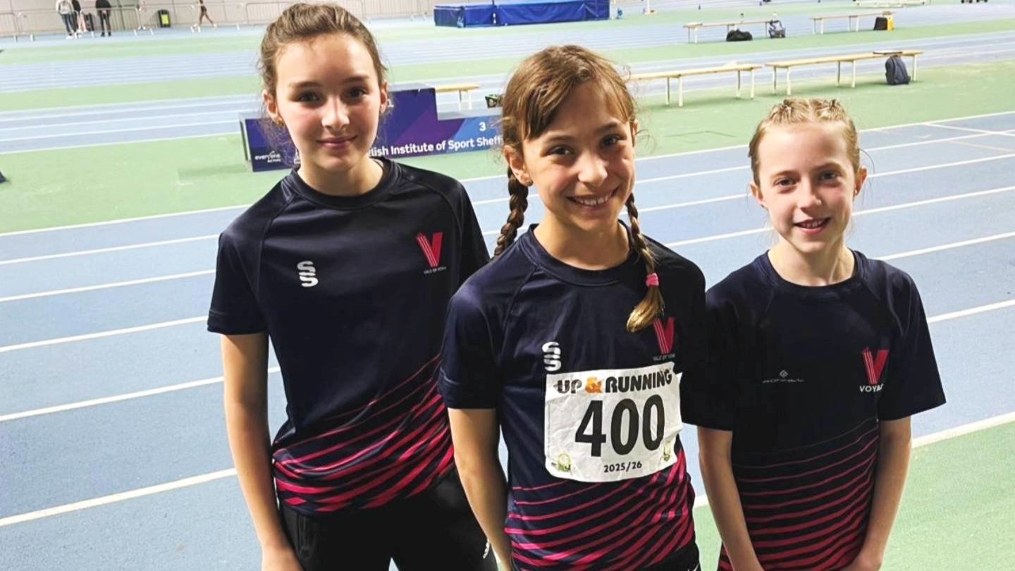 Three Vale of York junior athletes in club kit at the Sheffield indoor athletics track