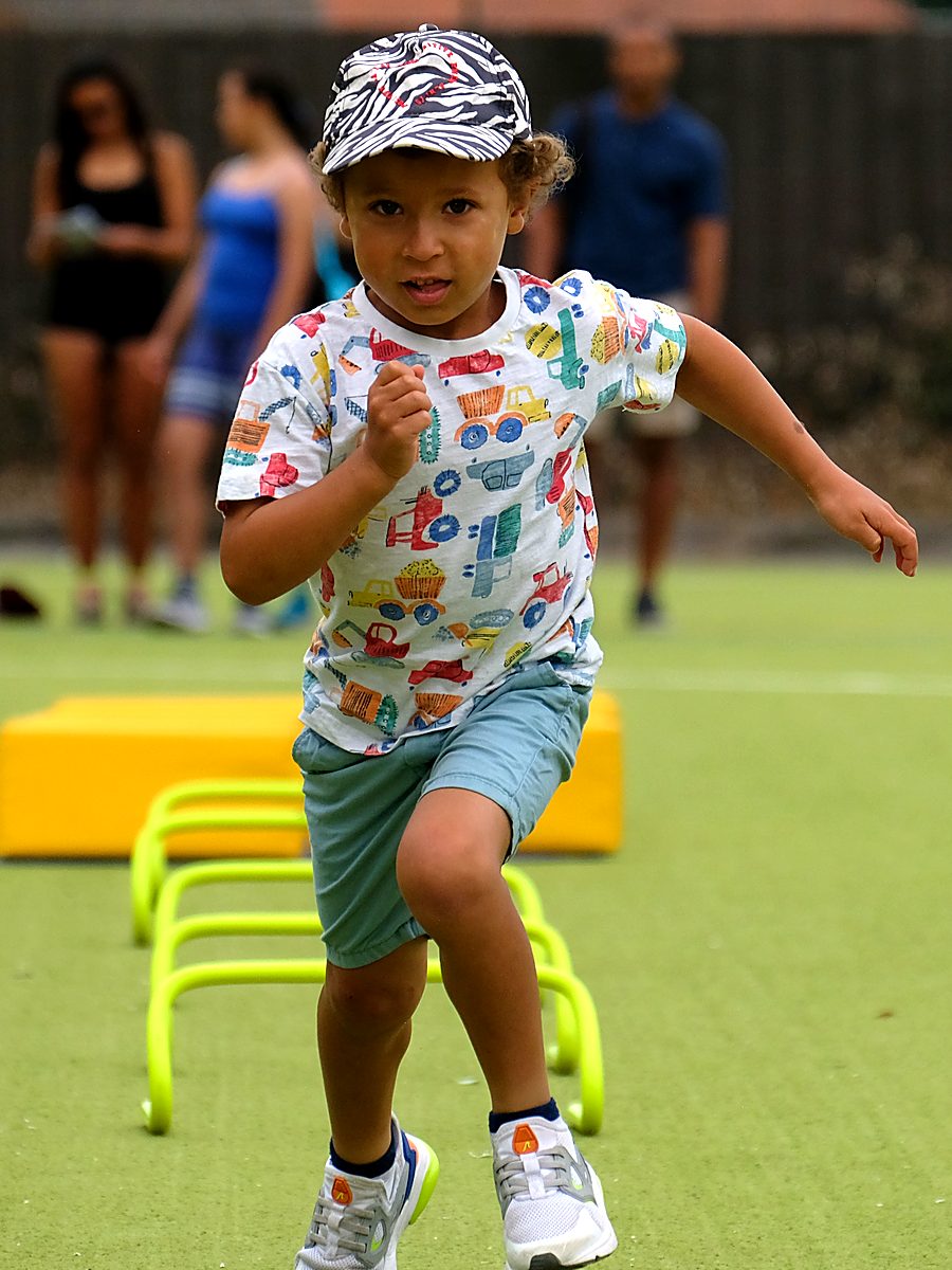 A young boy in a cap sprinting over mini hurdles at a Vale of York session