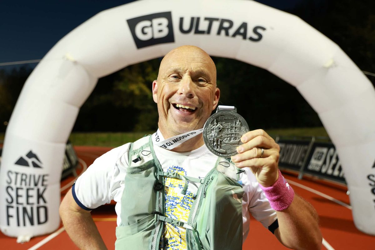 Adie Turford holding his finisher's medal under the GB Ultras arch at the end of the Glasgow to Edinburgh Ultra