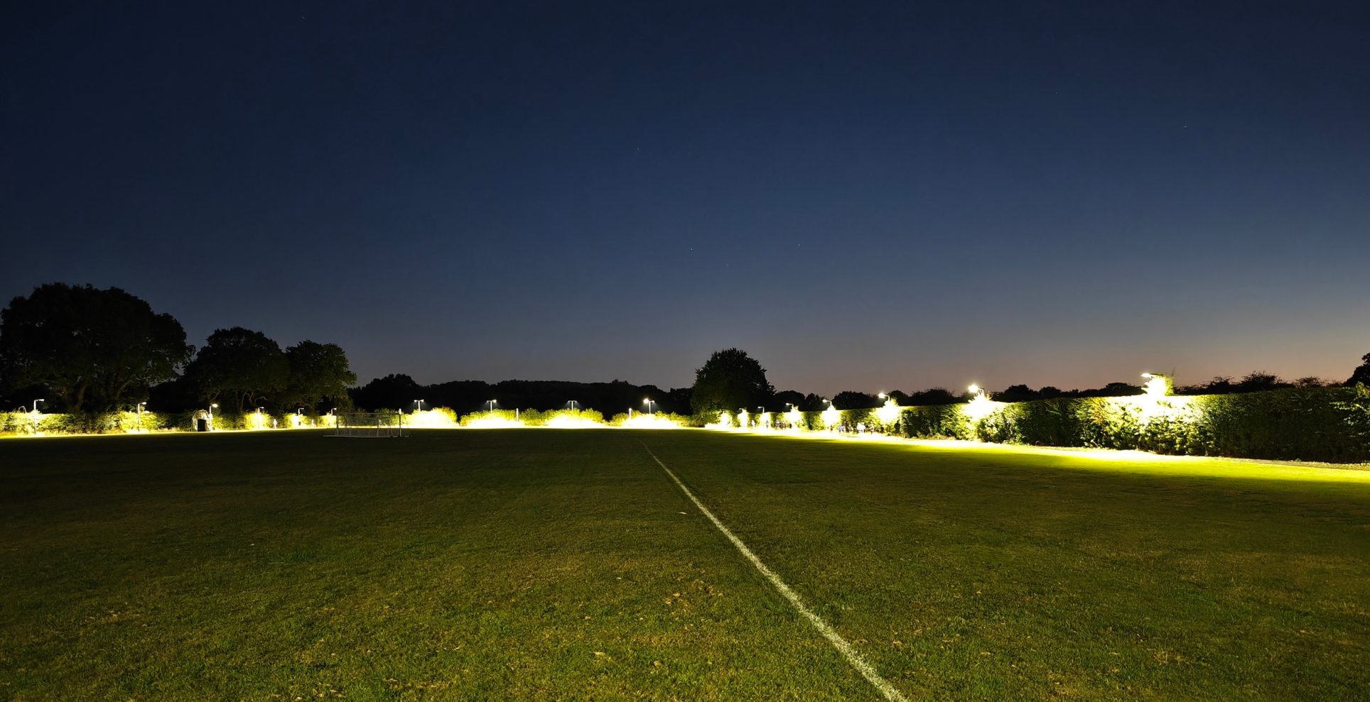 Floodlit grass circuit at Bubwith Leisure Centre at dusk, with runners training along the lit hedge line